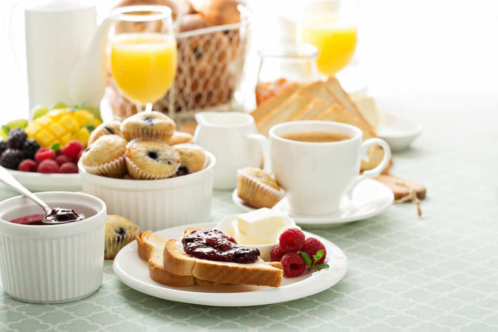Breakfast foods (toast, muffins, and fruit) and coffee on a table cloth.