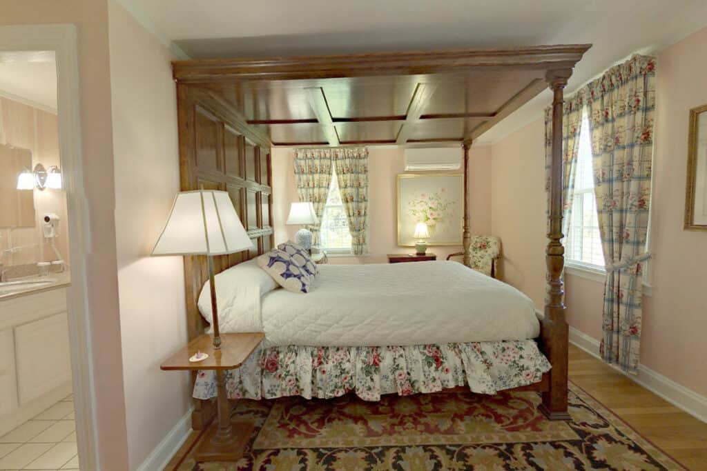 Beautiful wooden 4 poster bed with a side table and oriental carpet. Door to the bathroom is on the left.