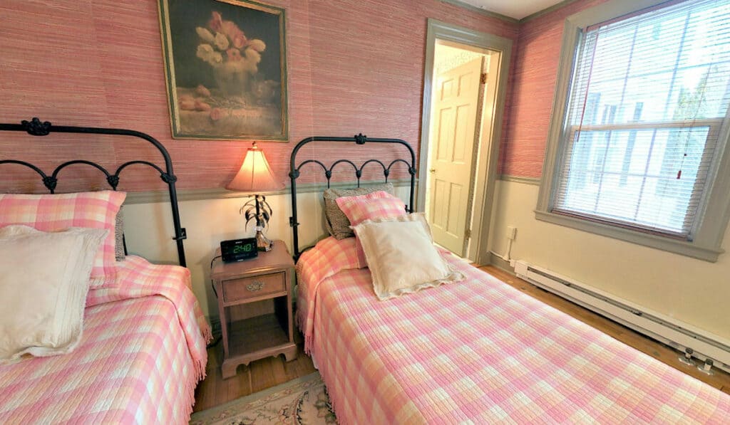two twin beds with pink plaid coverlets with a bedside table and lamp between them.