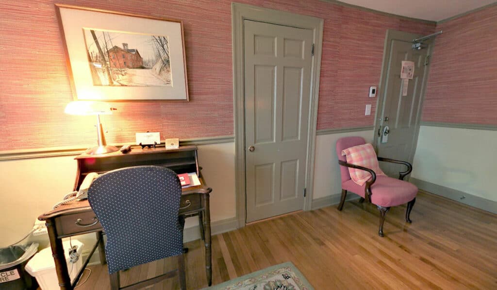The doors to the exit and bathroom. A desk with chair, an upholstered armchair.