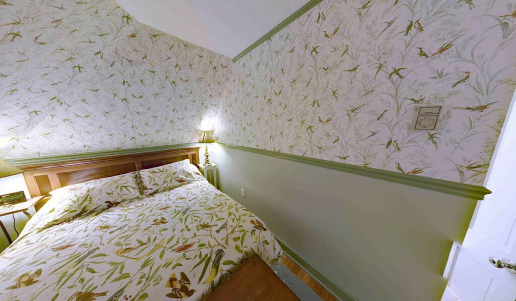 A closeup of the bed with bird print coverlet and similar bird print wallpaper